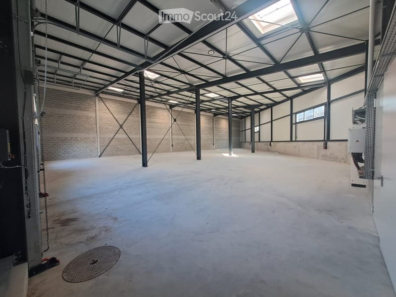 Empty industrial-style room with exposed metal beams, concrete floor, and large windows, featuring a manhole cover and air conditioning unit.
