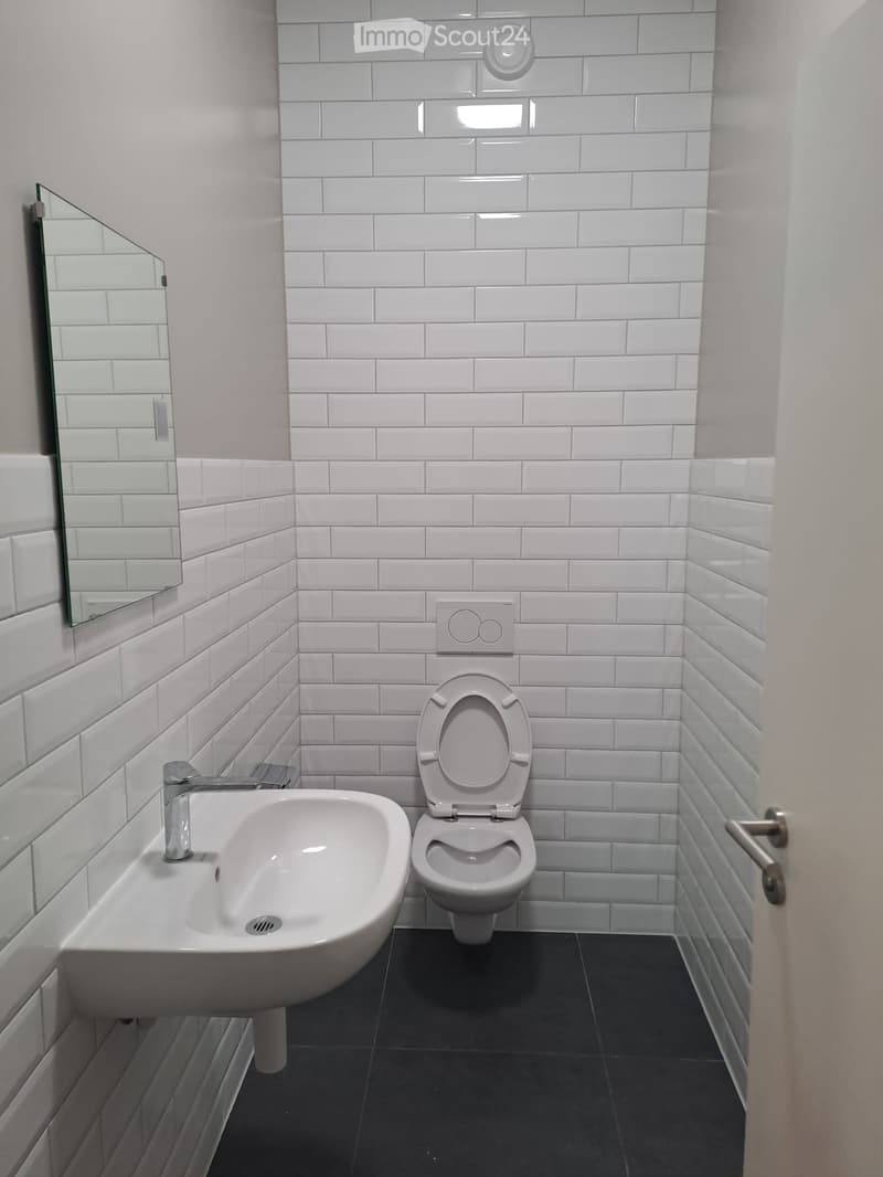 Modern bathroom with white tiled walls, a toilet, a sink with a chrome faucet, and a mirror on the wall.