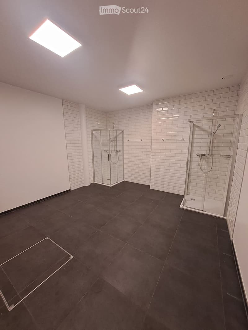 Modern bathroom with dark tiled floor, white brick walls, glass shower stall, and built-in shower area with multiple shower heads.