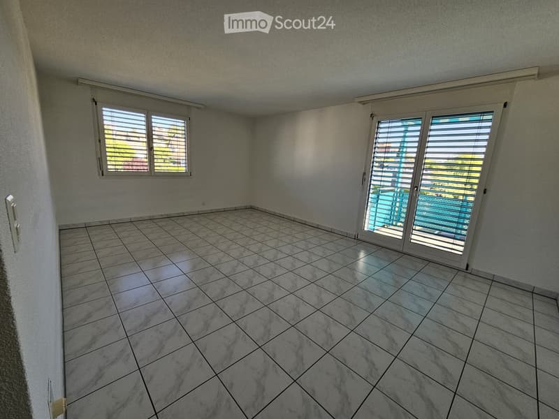 Empty room with tiled floor, white walls, and large windows with blinds. Features a sliding glass door leading to a balcony.