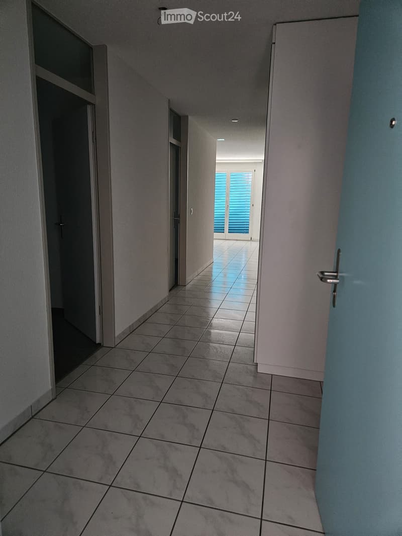 Empty hallway with tiled floor, grey walls, and several doors leading to other rooms.