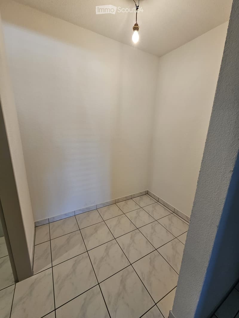 Empty room with tiled floor and white walls, featuring a single hanging light fixture.