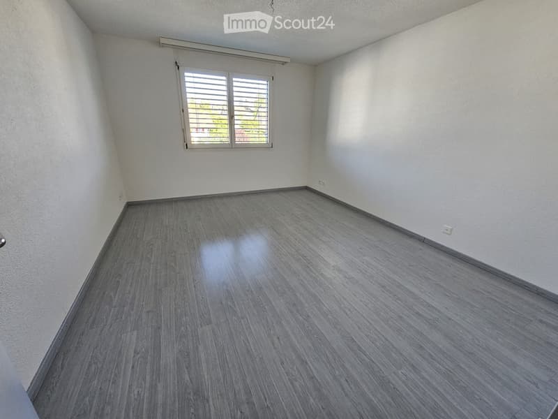 Empty room with light grey wooden flooring, white walls, and a single window with blinds. No furniture or equipment present.
