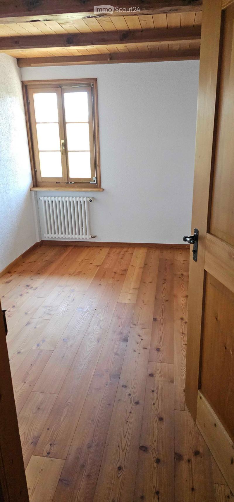 Empty room with wooden flooring, white walls, a window with wooden frame, and a radiator below it.