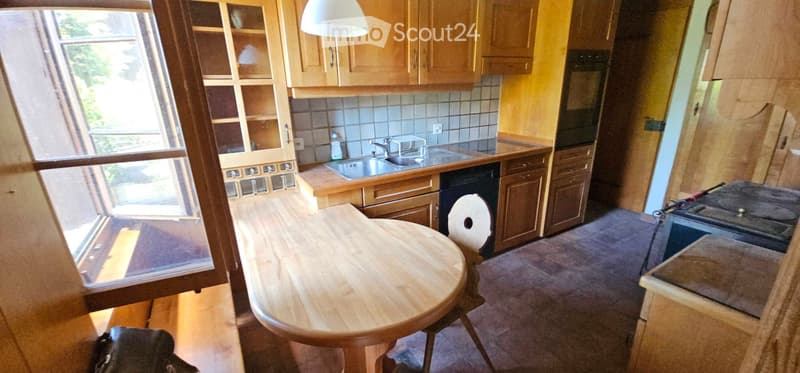 Bright kitchen with wooden cabinets, a sink, a dishwasher, and a round wooden dining table with a chair.