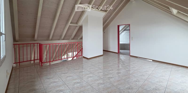 Empty room with exposed wooden beams on the ceiling, tiled floor, and a red metal railing leading to another area.