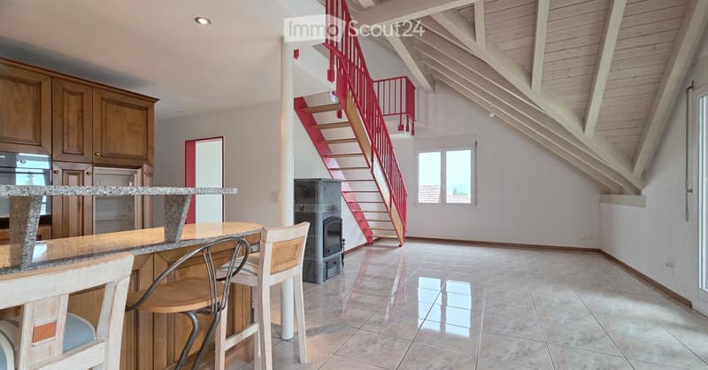 Open-plan living and dining area with a bar counter, wooden chairs, kitchen cabinets, and a red staircase leading to an upper level.