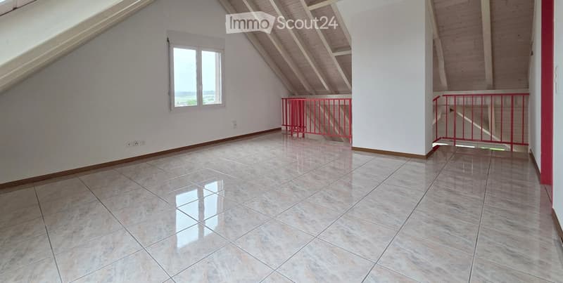 Empty room with tiled floor, white walls, and exposed wooden beams on the ceiling. Features a window and red safety railings.