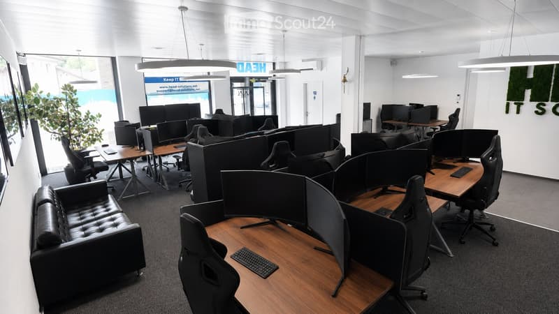 Modern office space with multiple workstations, ergonomic chairs, desks, computers, and a leather sofa in the foreground.