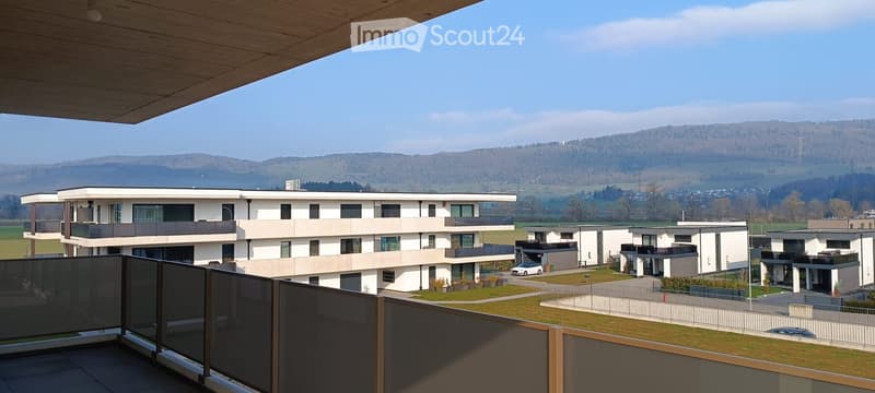Modern apartment building with balconies, surrounded by greenery, with a view of the mountains