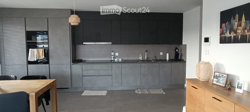 modern kitchen with gray cabinets, wooden table, black chairs, sink, oven, countertop, towels, picture frames