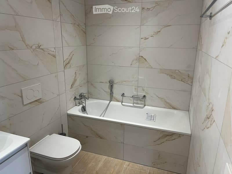 Bathroom with white marble tiles, bathtub, toilet, sink, and shower head