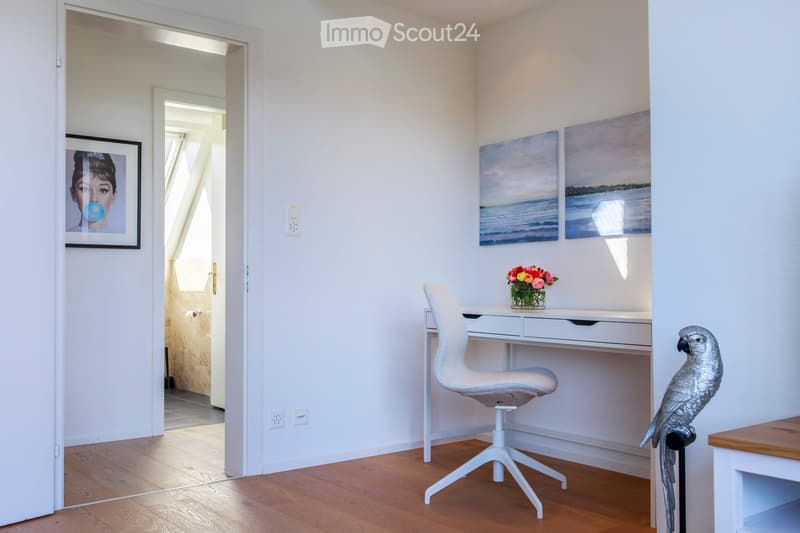 Bright, modern room with white walls, wooden floor, white desk, white chair, vase with flowers, and a decorative bird statue.