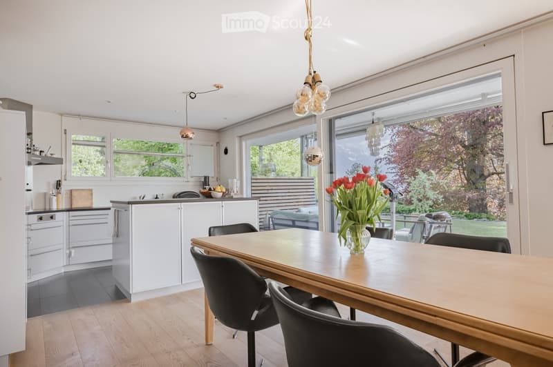 Modern kitchen with white cabinets, wooden dining table, and a view of the garden.