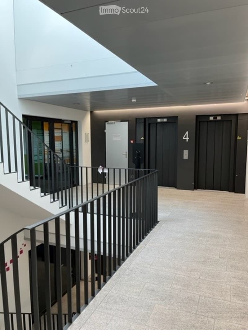 Modern interior corridor with a staircase, black metal railing, elevator doors labeled "4", and a glass-walled area on one side.