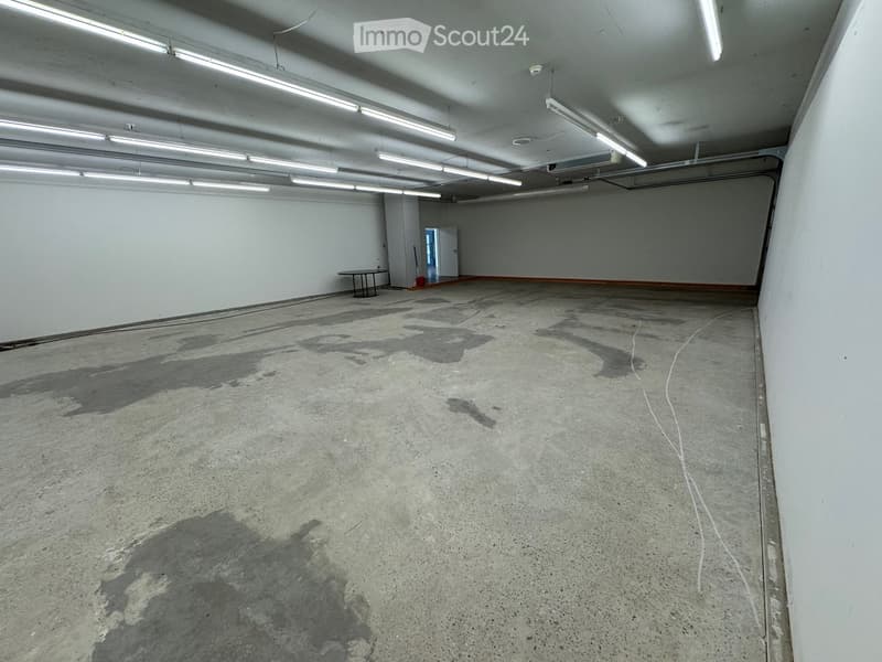 Empty room with concrete floor, white walls, fluorescent lighting, and a small table in the corner.