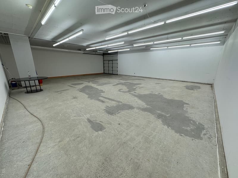Empty room with concrete floor, white walls, and fluorescent lighting. A small table and a few cleaning supplies are present.