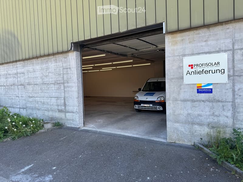 A modern building with a large garage entrance, featuring a white van inside and signage for "PROFISOLAR" and "Anlieferung".