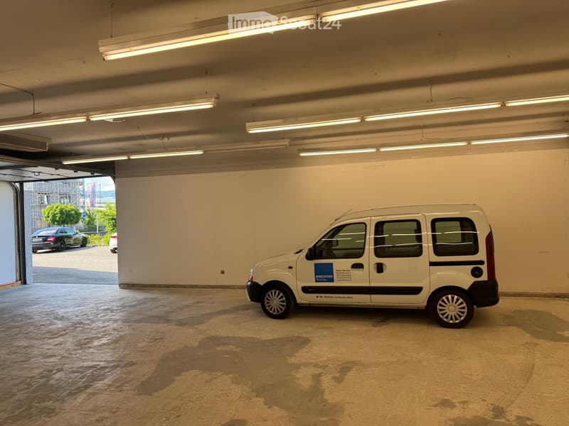 Underground garage with concrete floor, white walls, fluorescent lighting, and a parked white van.