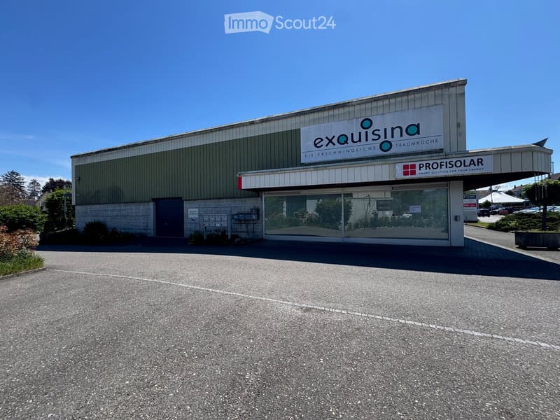 A modern commercial building with a sign reading "exquisina" and "PROFISOLAR" above the entrance, surrounded by a paved area with some greenery.