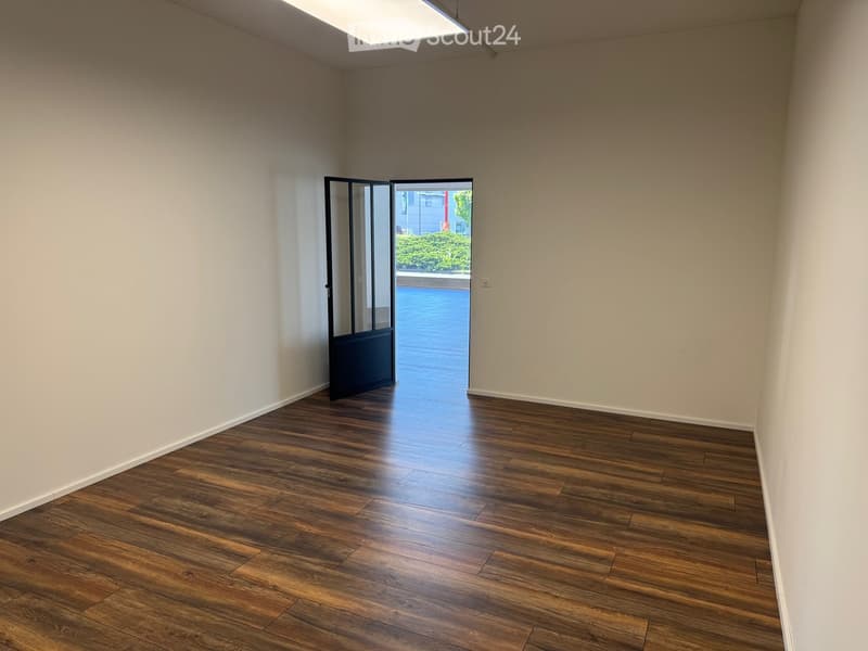 Empty room with wooden flooring and white walls, featuring a large open door leading to an outdoor area.