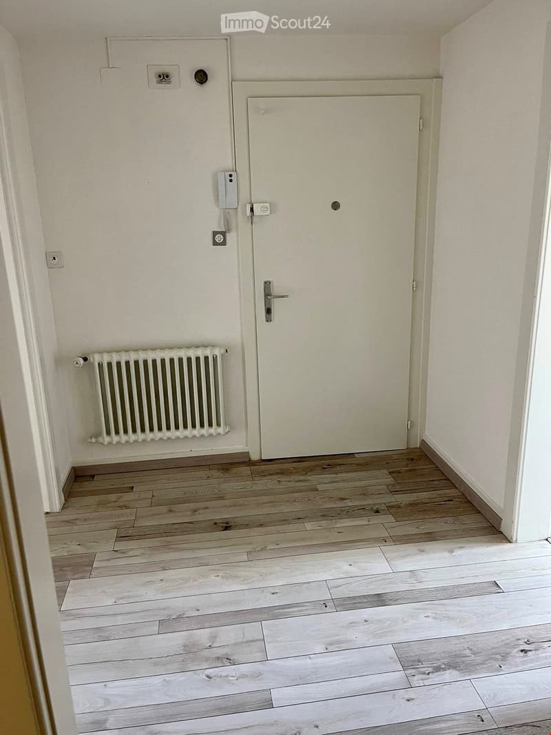 Empty hallway with wooden flooring, white walls, a closed door, and a radiator on the left side.