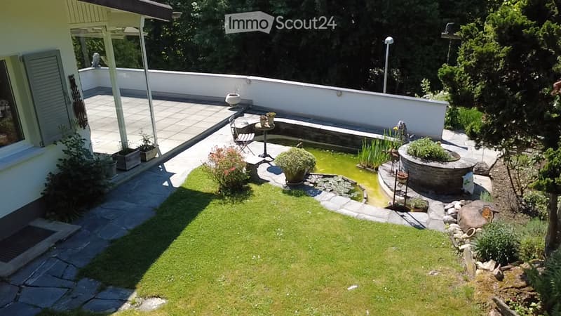 Garden / Outdoor Area. Well-maintained garden with a small pond, lush greenery, stone pathways, and a patio area with a table and chairs.