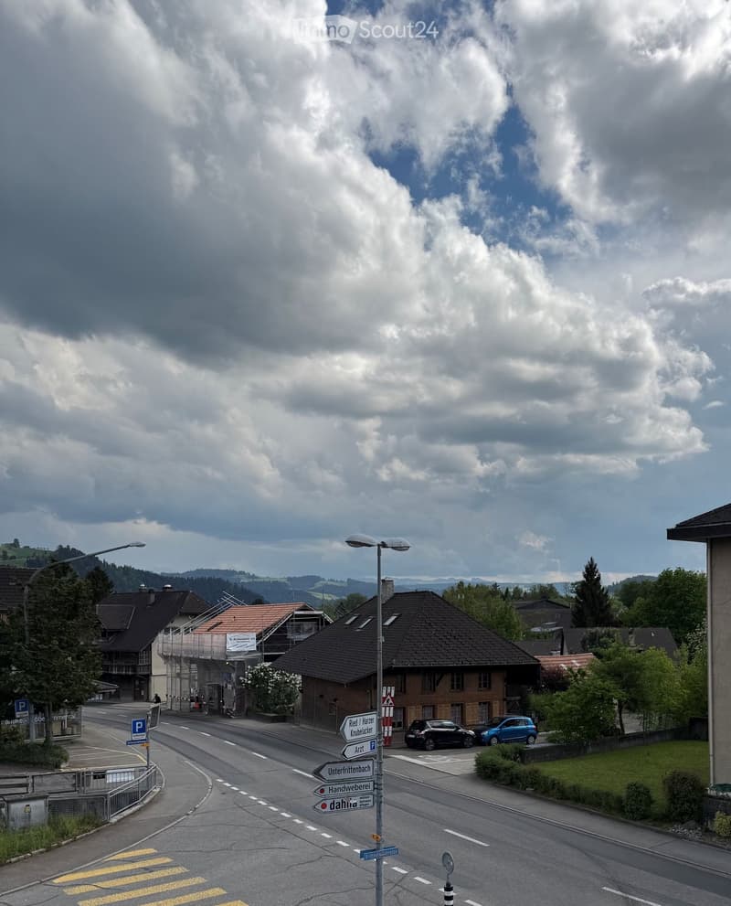 Residential street with houses, parked cars, street signs, and a cloudy sky.