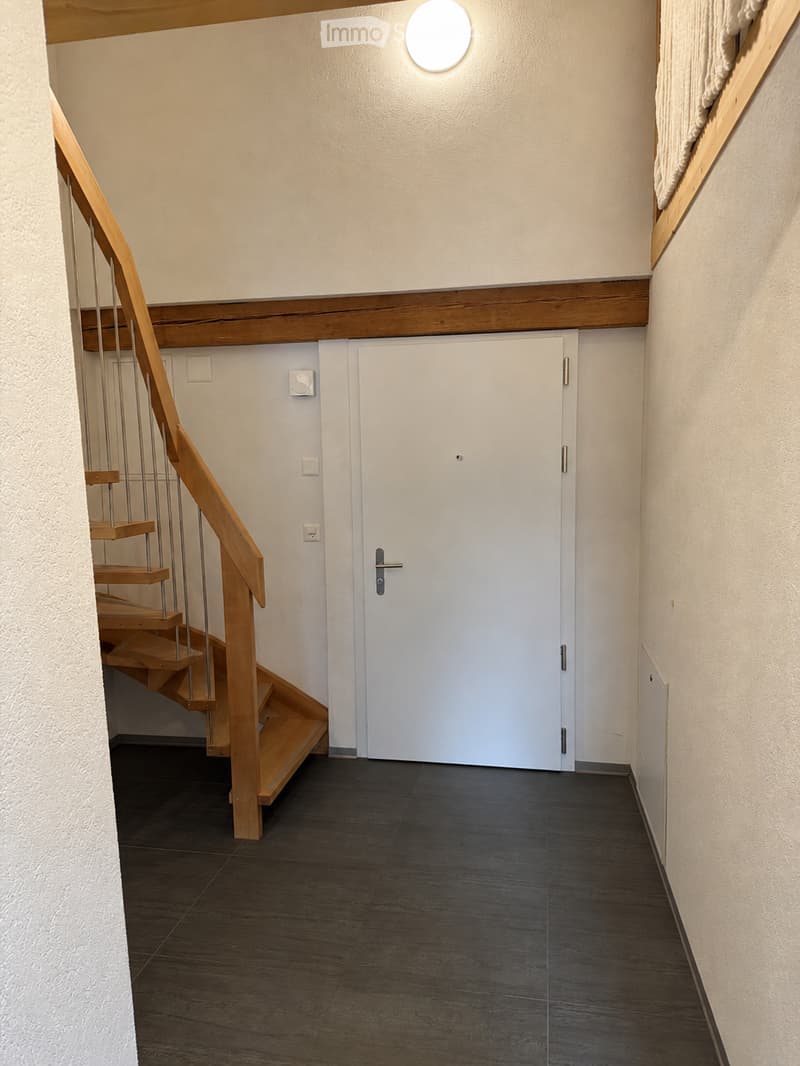 A modern hallway with a wooden staircase, dark tiled floor, white walls, and a closed white door.