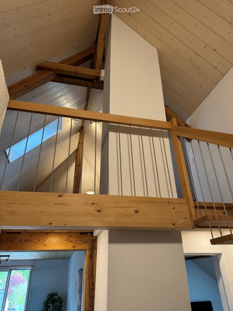 Wooden staircase with metal railings, exposed wooden beams, and a skylight above, leading to a lower level with a visible window and plant.