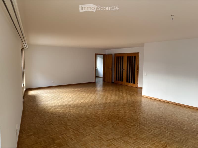 Empty room with wooden herringbone flooring, white walls, and two wooden doors leading to adjacent spaces.