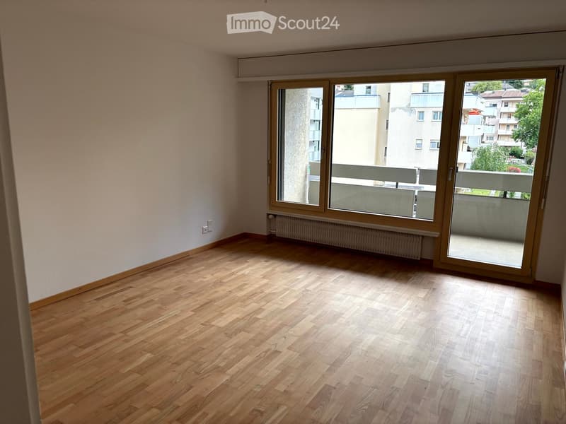 Empty room with wooden flooring, large windows, radiator, and sliding doors leading to a balcony.