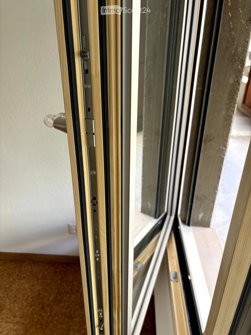 Close-up view of a modern sliding window with wooden frame and metal handle, showing the locking mechanism and glass panels.