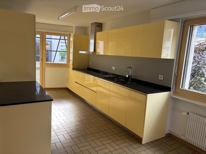 Modern kitchen with yellow cabinets, black countertops, tiled floor, and large windows offering a view of the outside.