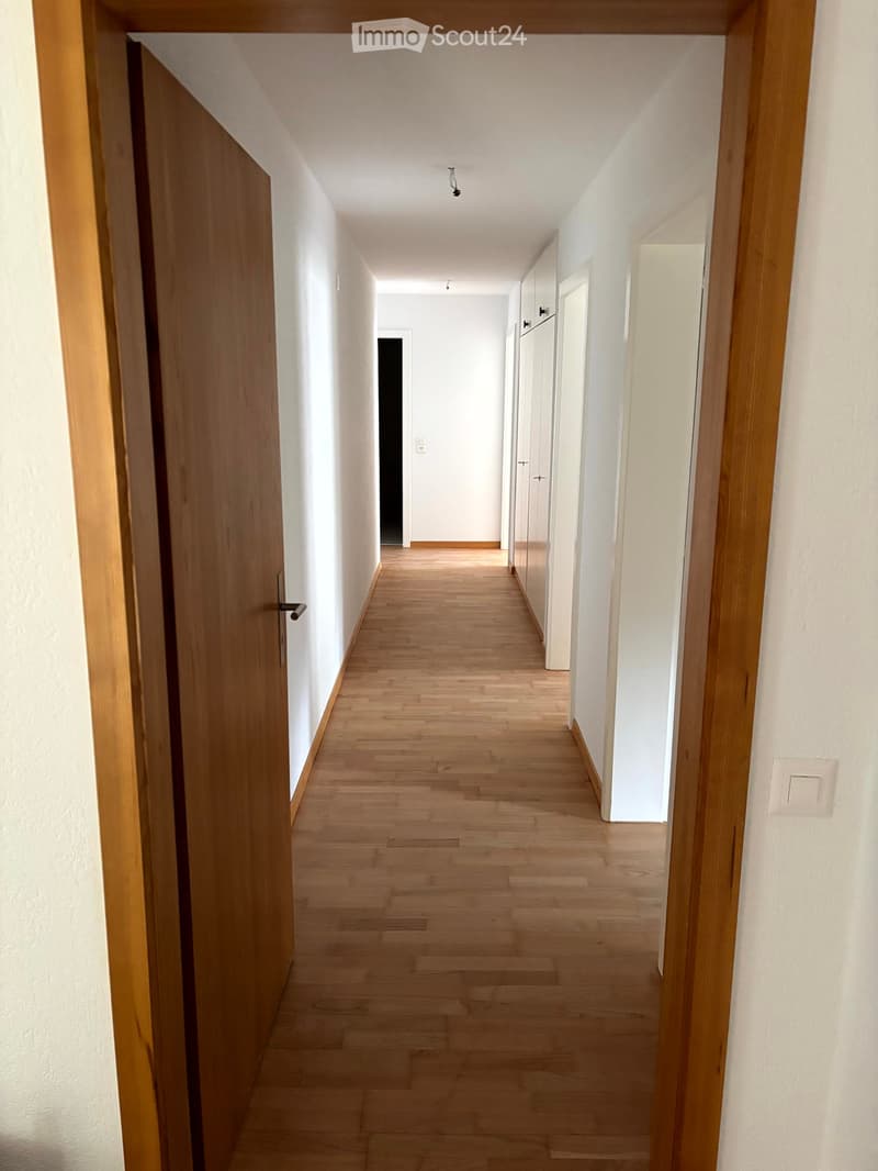 Empty hallway with light wooden flooring, white walls, and several closed doors along the sides.