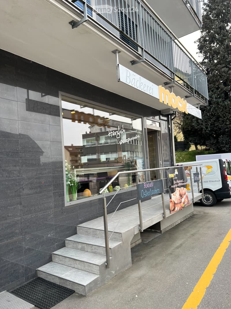 Bakery storefront with a staircase leading up to the entrance, featuring a sign for "Bäckerei Mock" and a display of pastries in the window.