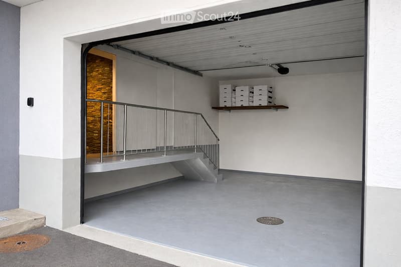 Modern, clean hallway with a raised ground floor, metal railing, and a small shelf holding white boxes.