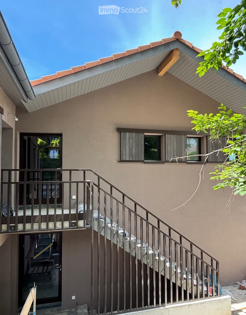 Two-story house with beige stucco walls, red-tiled roof, and multiple windows. A metal staircase leads to an upper-level balcony with a railing.
