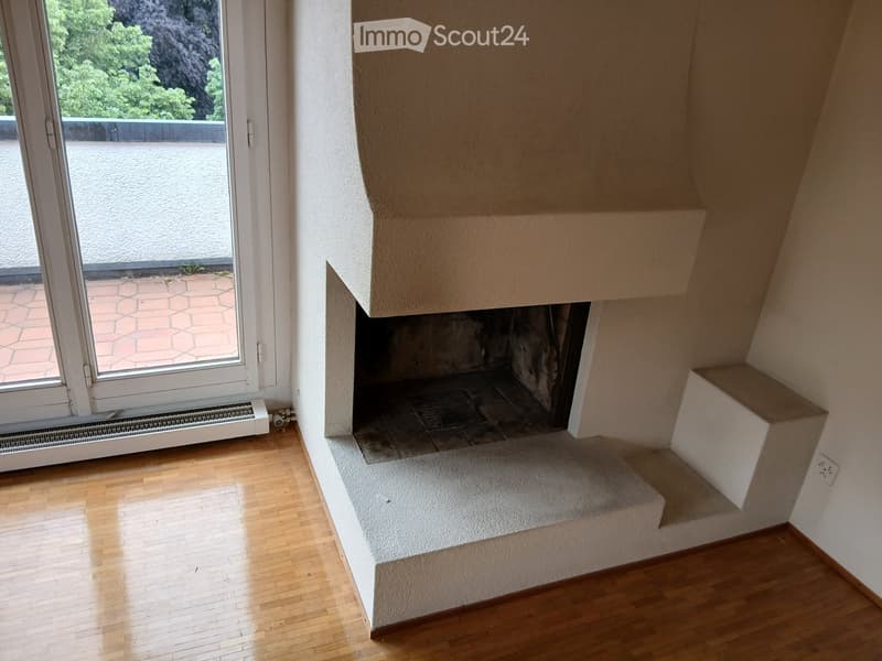An unfurnished room with wooden flooring, a fireplace, and a large window leading to a balcony area.