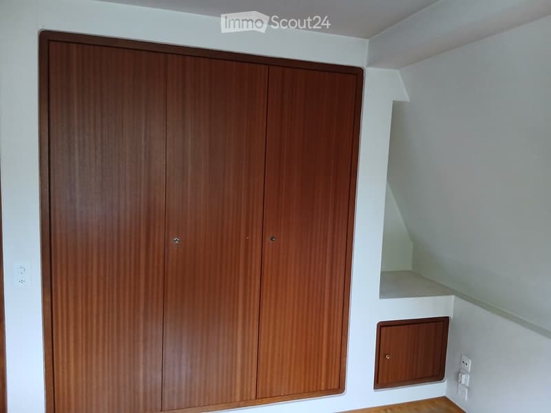 Empty room with white walls, wooden floor, and a large wooden closet with double doors.