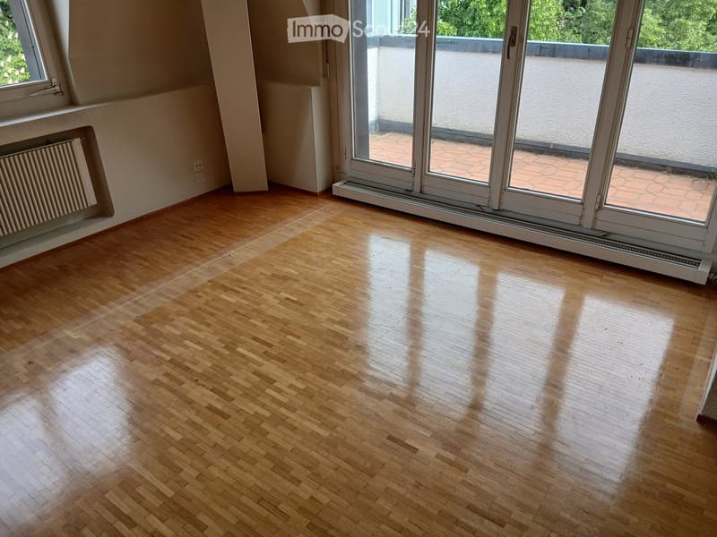 Empty room with wooden flooring, large sliding glass doors leading to a balcony, radiator, and a window on the left side.