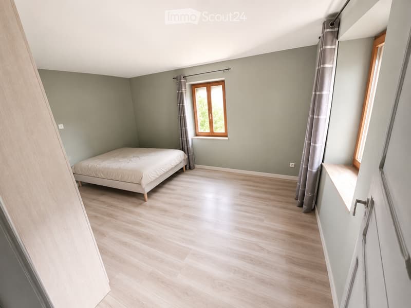 Bedroom. Bright bedroom with light green walls, wooden flooring, and a single bed with white bedding. The room features a window with wooden frame and grey curtains, and a small built-in shelf on the right side.