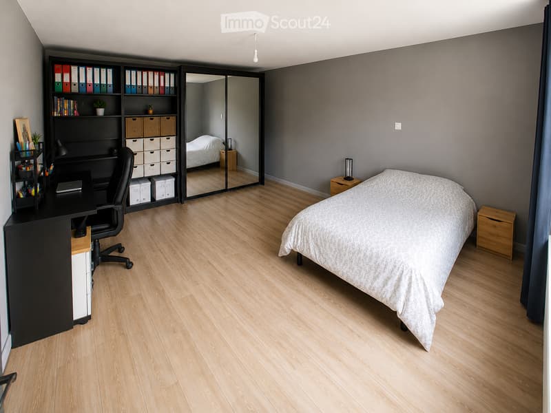 Bedroom. Modern bedroom with a large bed, wooden floor, black desk with chair, bookshelf with storage boxes, and a mirror reflecting part of the room.
