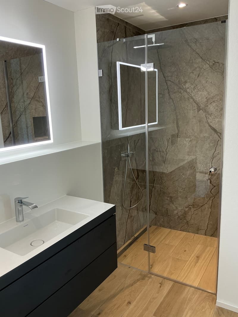 Modern bathroom with a white sink, black cabinet, glass shower enclosure, and marble-textured walls.