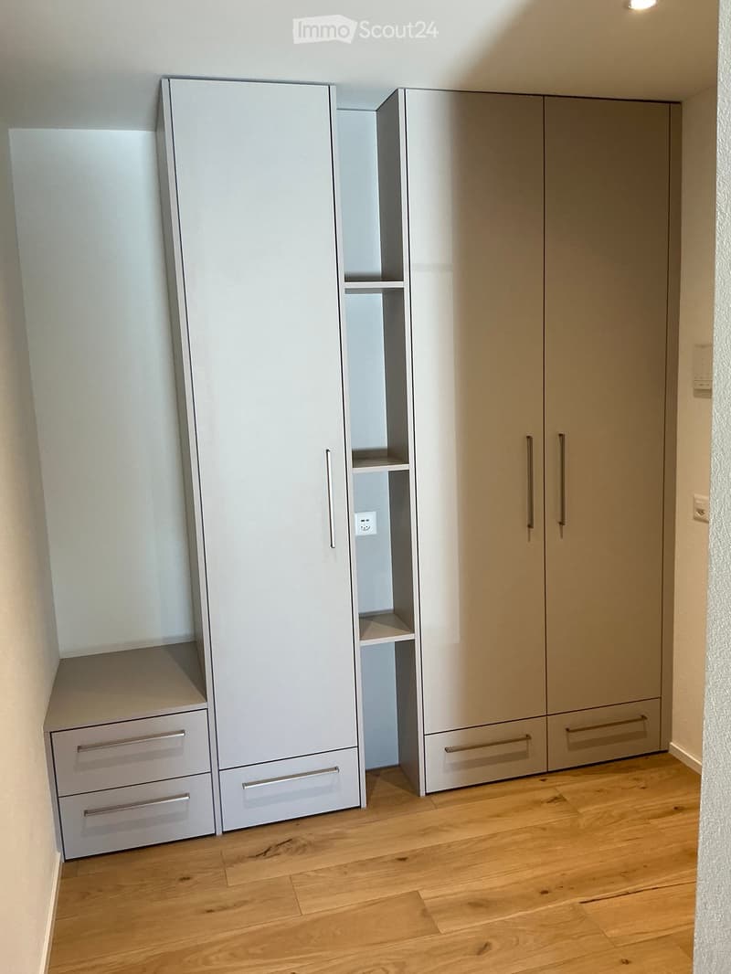 Empty room with light-colored wooden flooring and modern built-in wardrobes with multiple doors and drawers.