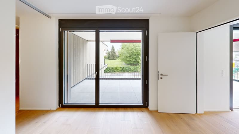 Empty room with wooden flooring, white walls, and a large glass door leading to an outdoor area.
