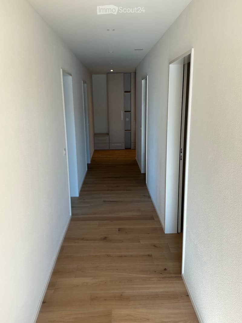 Empty hallway with wooden flooring, white walls, and several open doors leading to other rooms.