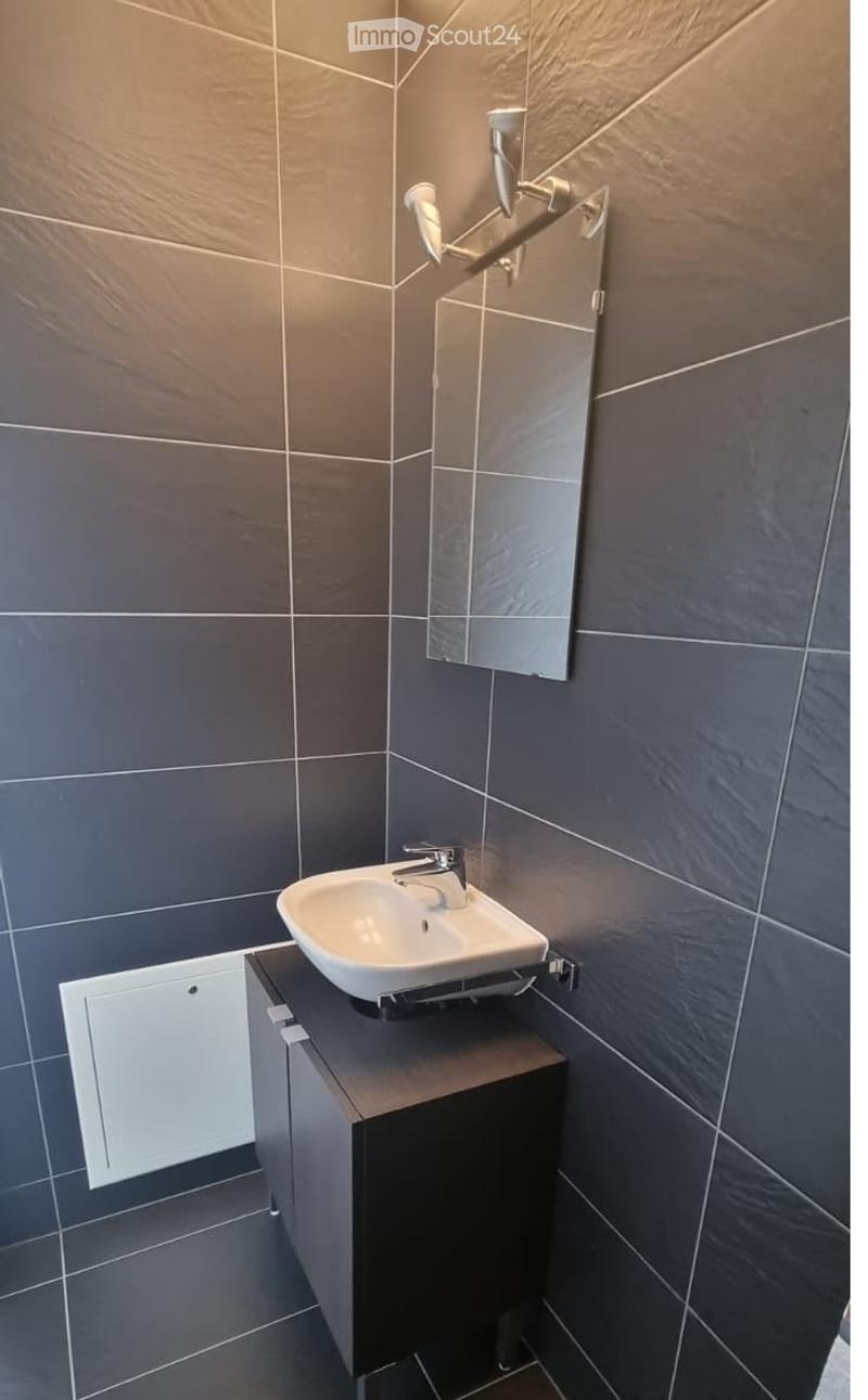 Modern bathroom with dark grey tiles, a white sink on a dark wooden cabinet, and a wall-mounted mirror with built-in lighting.