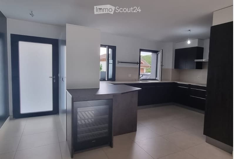 Modern kitchen with dark cabinets, a central island, and a built-in refrigerator. The space features large windows and a sleek, contemporary design.