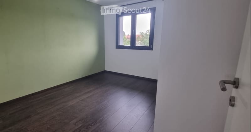 Empty room with wooden flooring, white walls, and a window with a view of trees.
